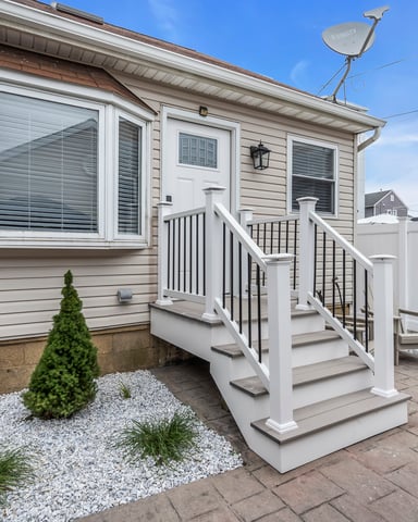 Modern mobile home exterior with white deck, large windows, and landscaped front yard with gravel and shrubs