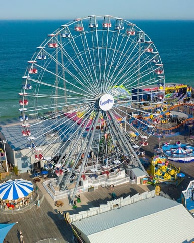 Aerial view of beachfront amusement park with Ferris wheel, roller coaster, and rides overlooking ocean