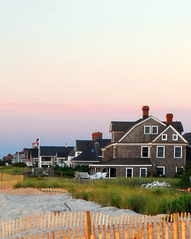 Beachfront homes at sunset with wooden dune fences and American flag on sandy shore