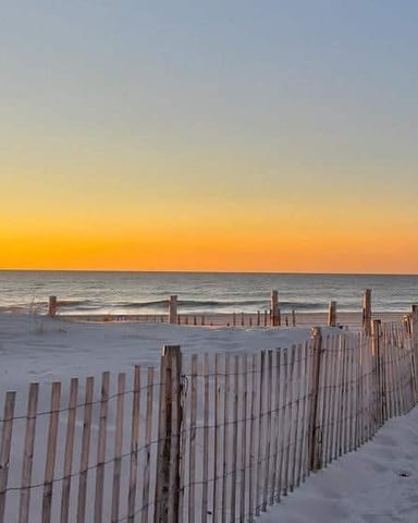 Sandy beach at sunset with wooden dune fences and ocean horizon under golden sky