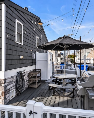 Deck with black umbrella, picnic table, grill, and string lights overlooking residential neighborhood