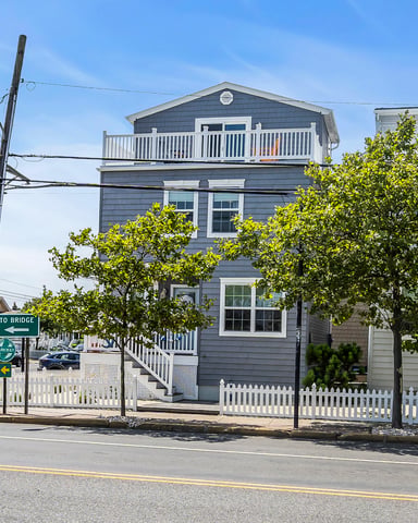 Gray shingled house with white railings and deck on residential street near bridge sign