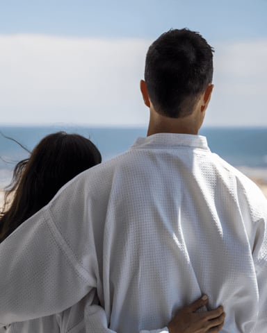 Couple in white shirt viewing sandy beach and ocean from grassy overlook