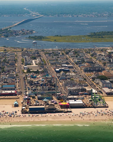 Aerial view of Jersey Shore boardwalk with amusement park, sandy beach, and bay with bridge in distance
