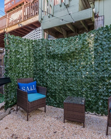 Patio with gas grill, wicker chairs with blue cushions, ivy-covered privacy screen, and wooden decks above