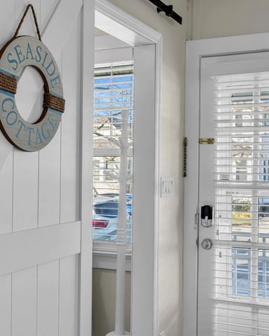 Entryway with white shiplap door, seaside cottage rope wreath, and shuttered glass door with ocean view