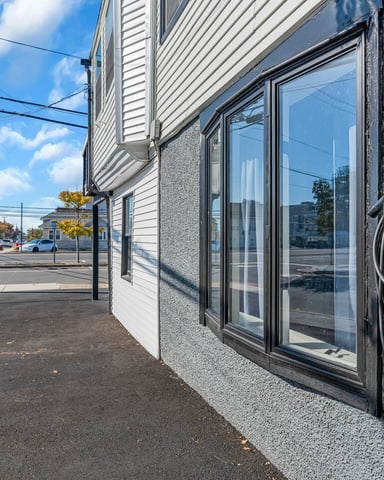 Modern storefront with large windows and electric vehicle charging cable mounted on textured gray wall, street view with stop sign and residential buildings