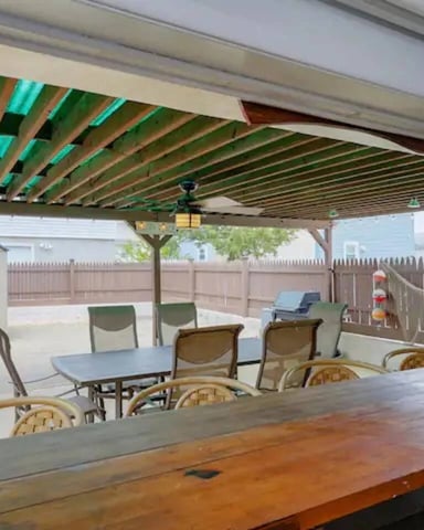 Covered patio with green pergola, dining table, lounge chairs, and fenced backyard with garage and shed