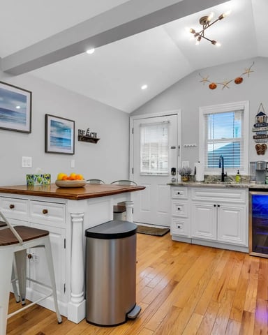 Modern kitchen with white cabinetry, wood countertop island, stainless steel appliances, and ocean views through windows