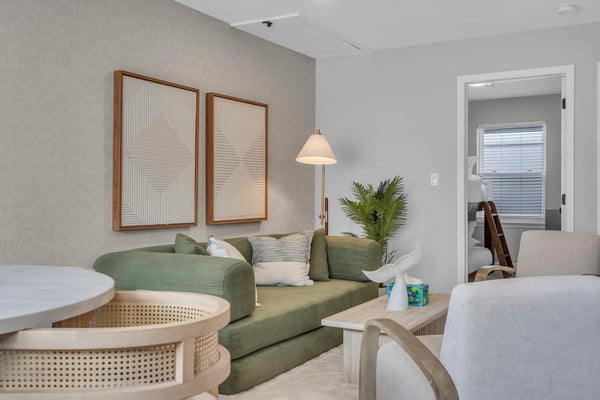 Modern living room with green curved sofa, geometric wall art, brass floor lamp, potted plant, and light wood furniture
