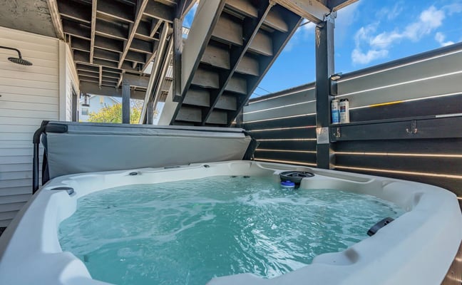 Hot tub with turquoise water on covered deck with metal pergola and black privacy fence