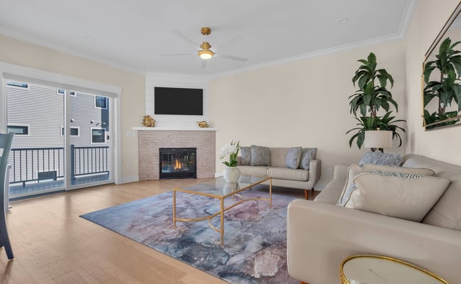 Bright living room with fireplace, cream sofas, glass coffee table, potted plants, and deck access through sliding doors
