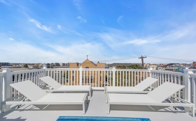 Rooftop deck with white lounge chairs and railing overlooking residential neighborhood and church building