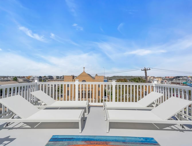 Rooftop deck with white lounge chairs and railing overlooking residential neighborhood and church